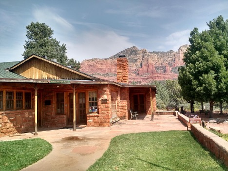 Sedona Heritage Museum building made of red rock with chimney, green lawn, and red rock cliffs in the background.